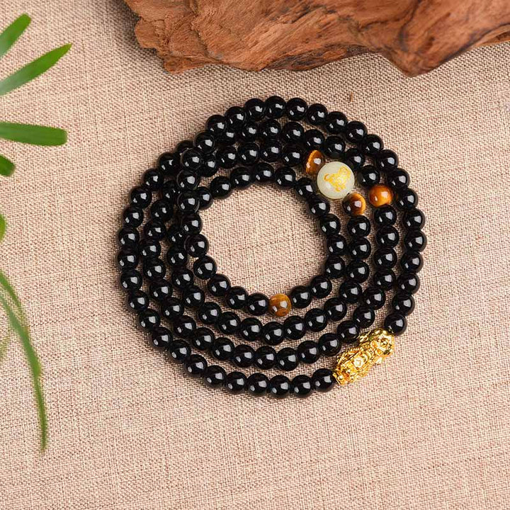 Schwarzes Obsidian Armband mit goldenen Akzenten auf Leinenstoff Untergrund