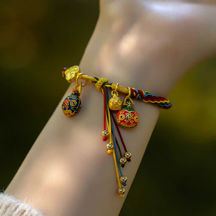 Goldenes Armband mit bunten Anhängern am Handgelenk getragen.