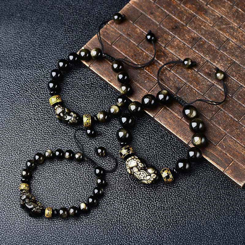Schwarze Obsidian Armbänder mit goldenen Om Mani Padme Hum Anhängern elegant arrangiert.