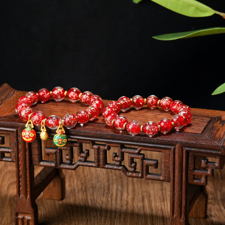 Rotes Perlenarmband mit goldenen Charms auf Holzständer.