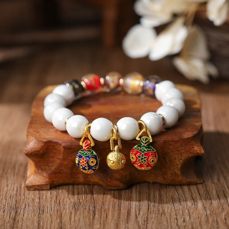 Weißes Perlenarmband mit vergoldeten Glückscharm-Anhängern elegant.