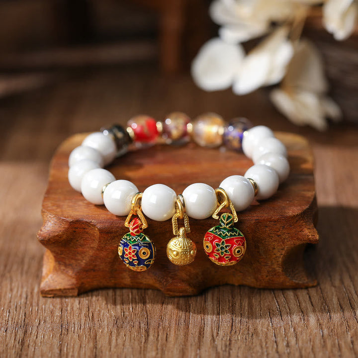 Weißes Perlenarmband mit vergoldeten Glückscharm-Anhängern elegant.