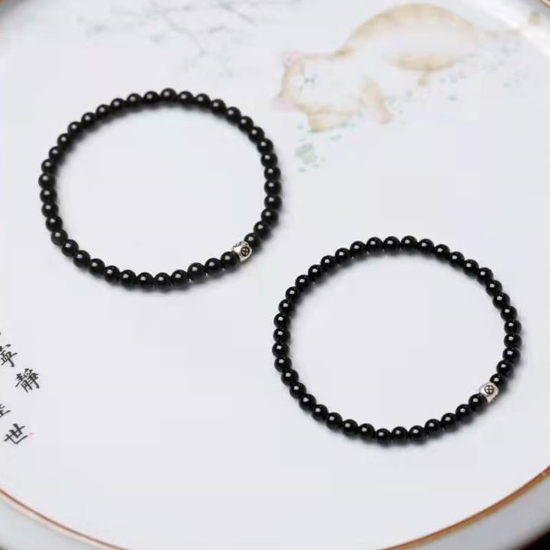 Zwei schwarze Obsidian Armbänder mit Katzen-Charm auf weißem Untergrund