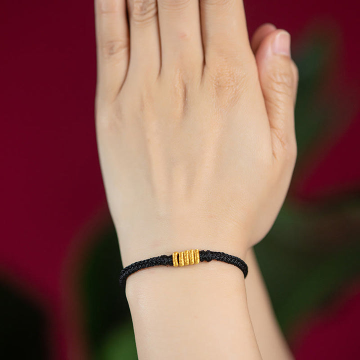 Schwarzes geflochtenes Armband mit goldenem Verschluss am Handgelenk getragen