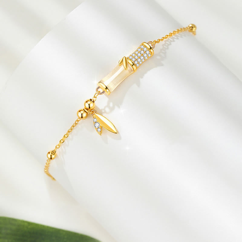 Goldenes Armband mit Zylinder-Anhänger und Blatt-Charm elegant präsentiert.