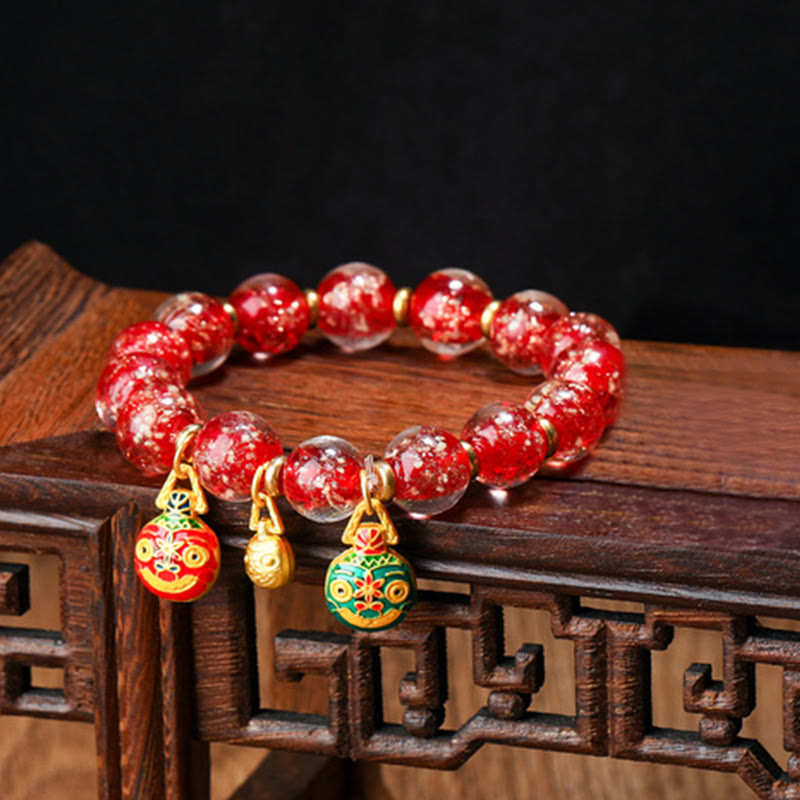 Rotes Armband mit Goldanhängern auf Holzoberfläche elegant präsentiert.