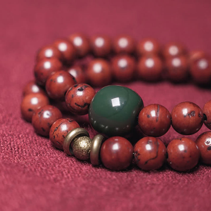 Armband Cyan Jade Kupfer mit roten Perlen auf rosa Untergrund.
