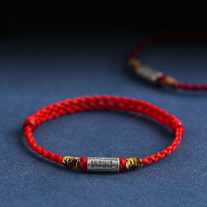 Rotes Armband mit Silber-Anhänger auf blauem Hintergrund, elastisch, Schutz & Stärke
