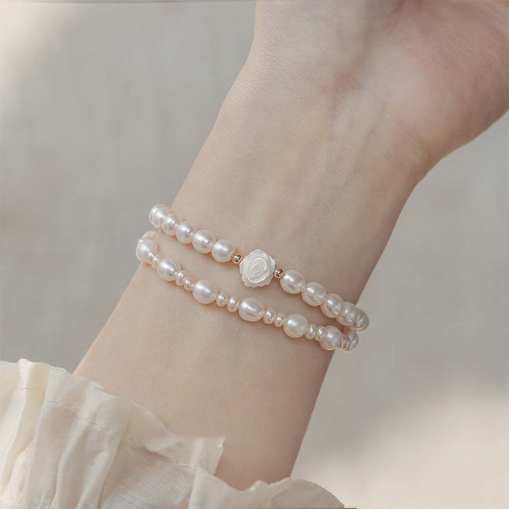 Elegantes Perlenarmband mit weißer Blume am Handgelenk getragen.