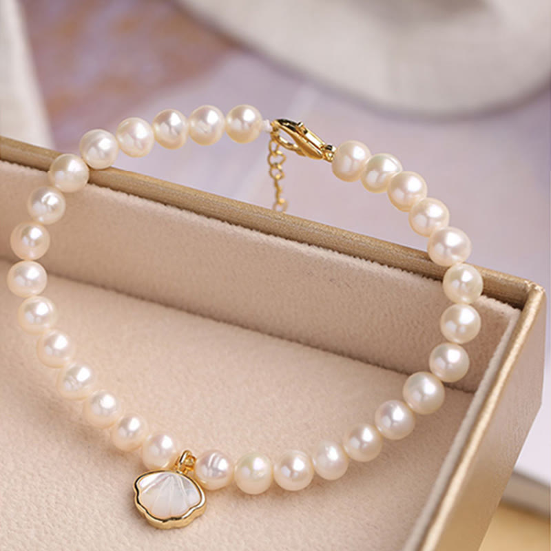 Elegantes Perlenarmband mit Muschelanhänger auf beigem Display.