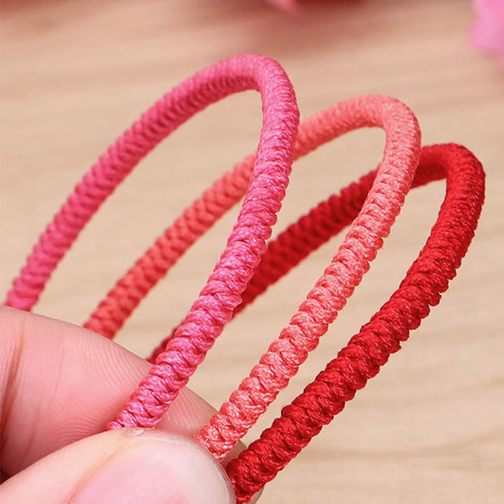 Drei geflochtene Armbänder in Rosa- und Rottönen am Handgelenk.