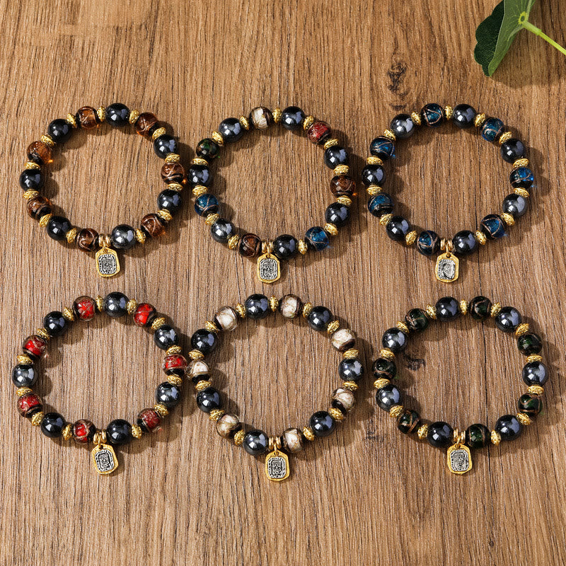 Sechs bunte Armbänder mit schwarzen Perlen und goldenen Spacern auf Holz.