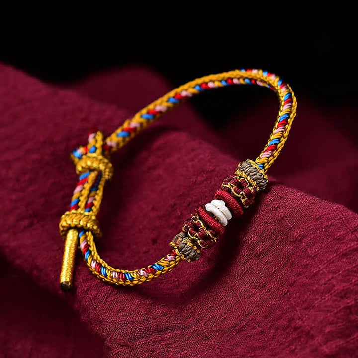 Geflochtenes rotes Schnur Karma Armband mit goldenen Verzierungen auf burgunderrotem Stoff.
