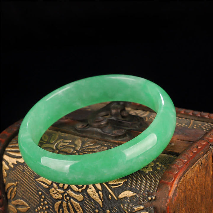 Grünes Jade Armband auf Holzschatulle mit Blumenmotiv elegant präsentiert.
