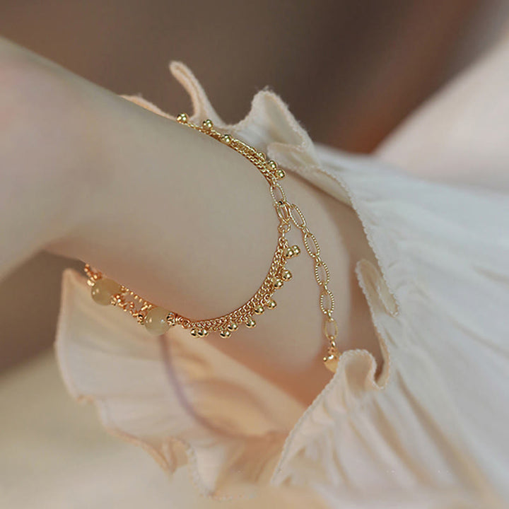Goldenes Armband mit Anhängern auf weißer Blüte elegant draped.