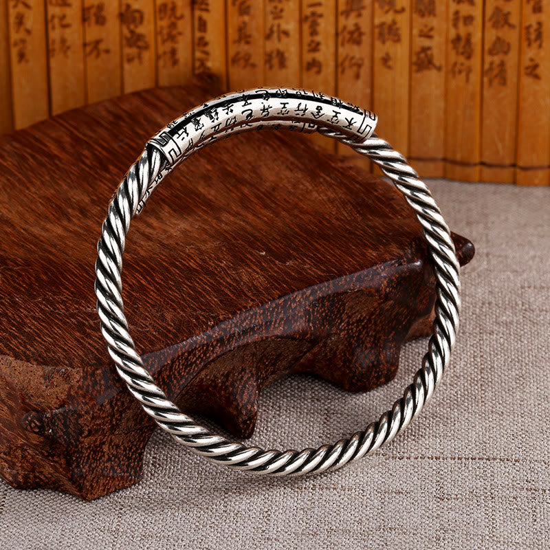 Silbernes Herzsutra Armband mit gedrehtem Design auf Holz.