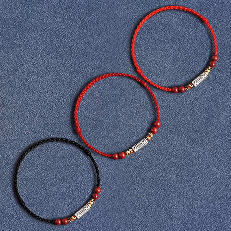 Drei rote und schwarze Armbänder mit goldfarbenen Perlen auf grauem Hintergrund.
