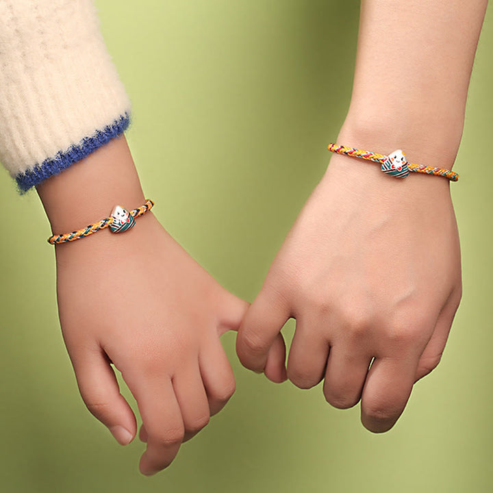 Zwei Kinder halten Hände mit farbenfrohen Drachen-Armbändern aus Silber.