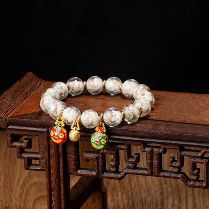 Weißes Perlenarmband mit goldfarbenen Charms auf Holzoberfläche.