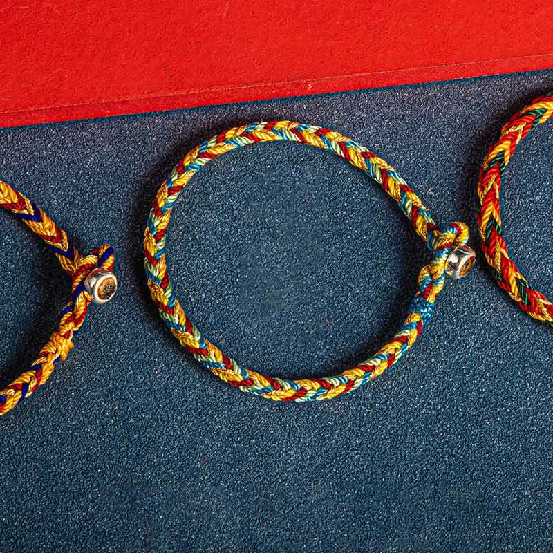 Mehrfarbiges Armband mit Glückssymbolen auf dunklem Stoff, elastisch, Flachaufnahme.