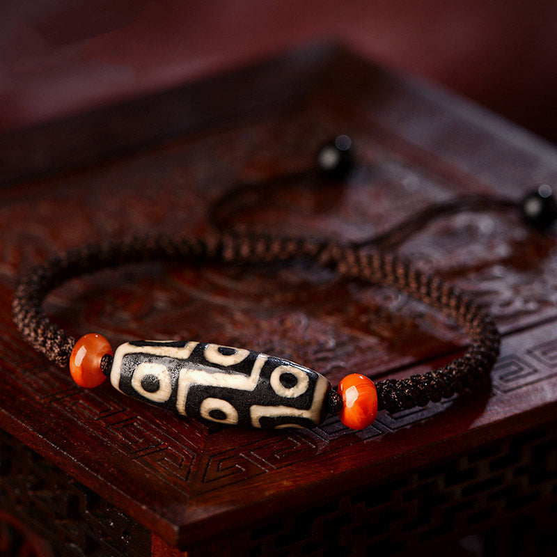 Dzi-Perle Neun Augen Armband mit roten Achatsteinen auf Holzoberfläche, Wohlstand Prosperität.