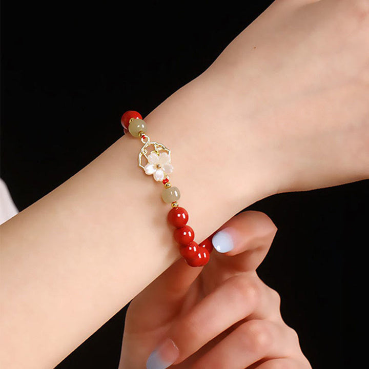Armband Zinnober Jade – Segen mit weißer Blüte am Handgelenk getragen
