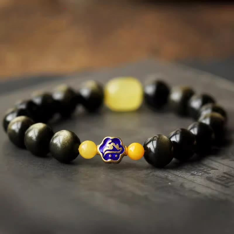 Schwarzes Obsidian Armband mit gelbem Stein und blauem Tierkreis-Charm elegant präsentiert.
