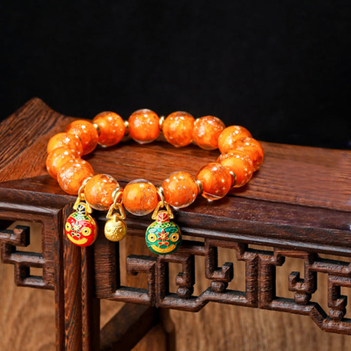 Oranges Perlenarmband mit vergoldeten Glücksbringern auf Holz.