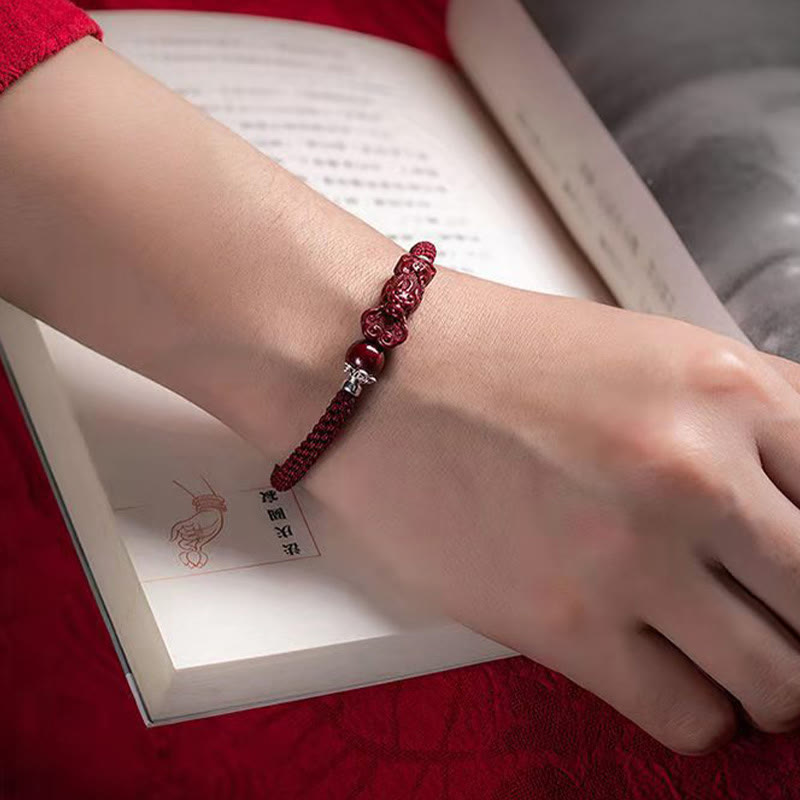 Zinnober Pixiu Armband am Handgelenk über Buch rotes elastisches Armband Glück