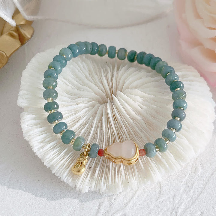 Grünes Jade Armband mit goldenen Charms auf weißer Bürste präsentiert.