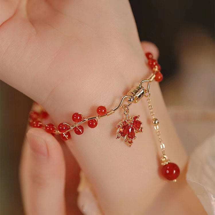 Rotes Armband mit Ahornblatt-Charm und Glücksperlen am Handgelenk.
