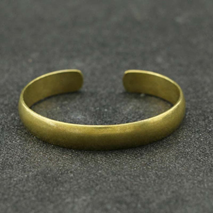 Goldenes offenes Armband mit matter Oberfläche auf grauem Hintergrund.