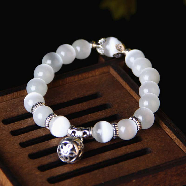 Weißes Mondstein Armband mit silbernem Anhänger auf Holz.