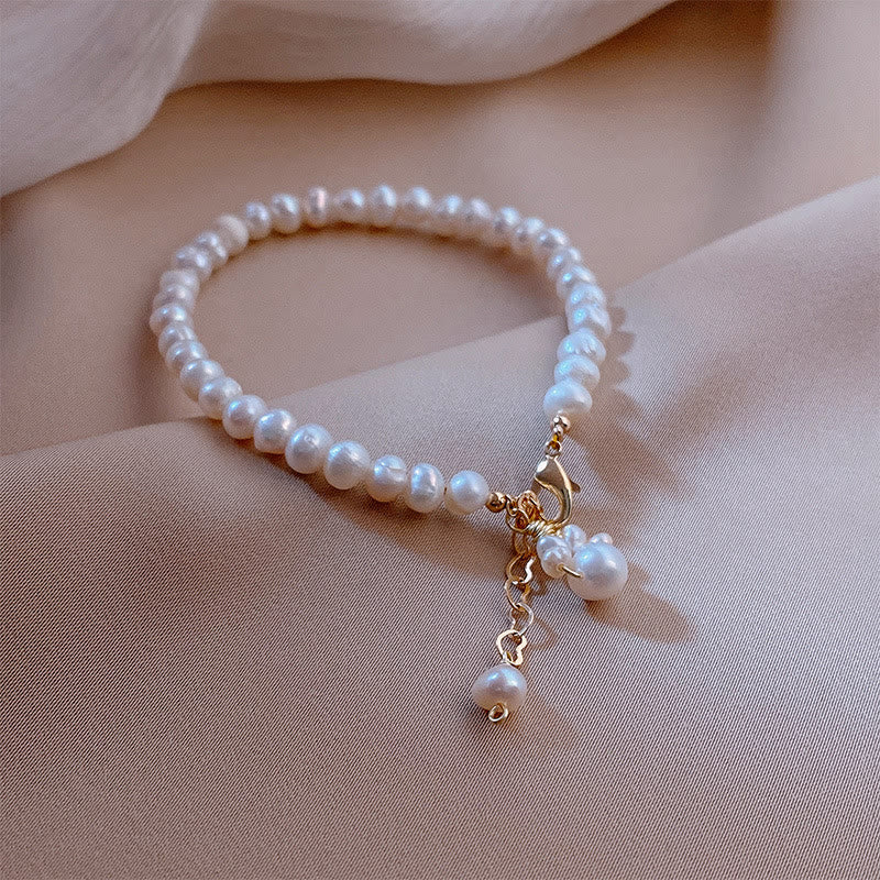 Elegantes Perlenarmband mit Katzenamulett und goldenem Verschluss am Handgelenk getragen.