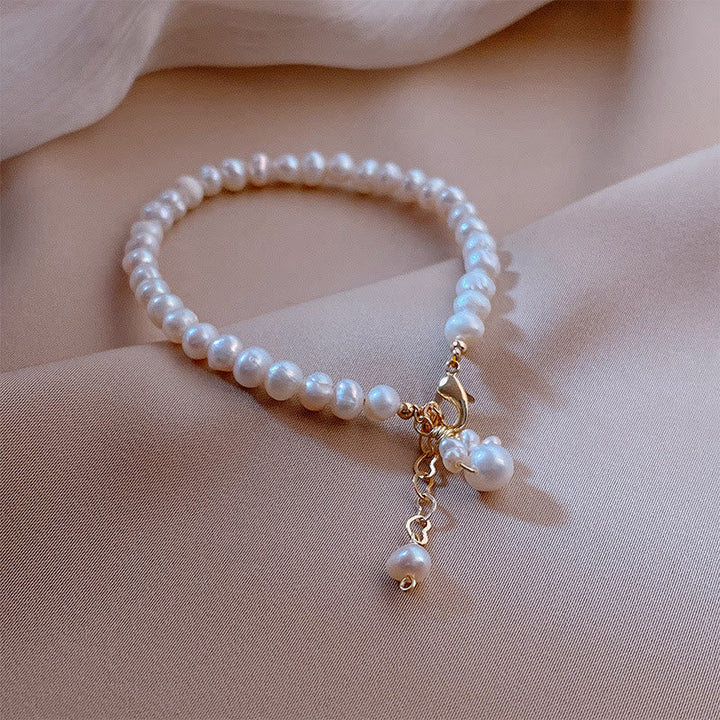 Elegantes Perlenarmband mit Katzenamulett und goldenem Verschluss am Handgelenk getragen.