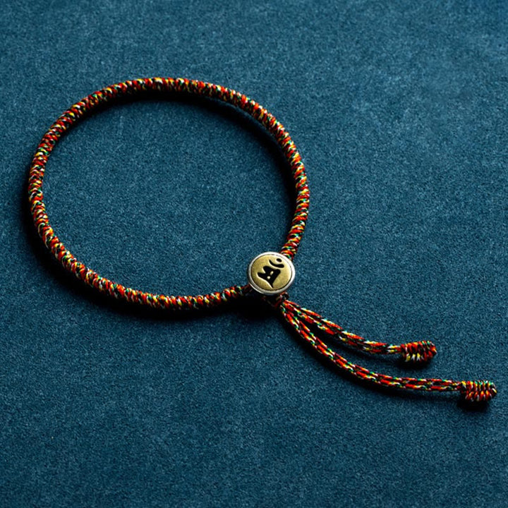 Rotes Armband mit goldenem Tierkreis-Charm auf blauem Hintergrund.