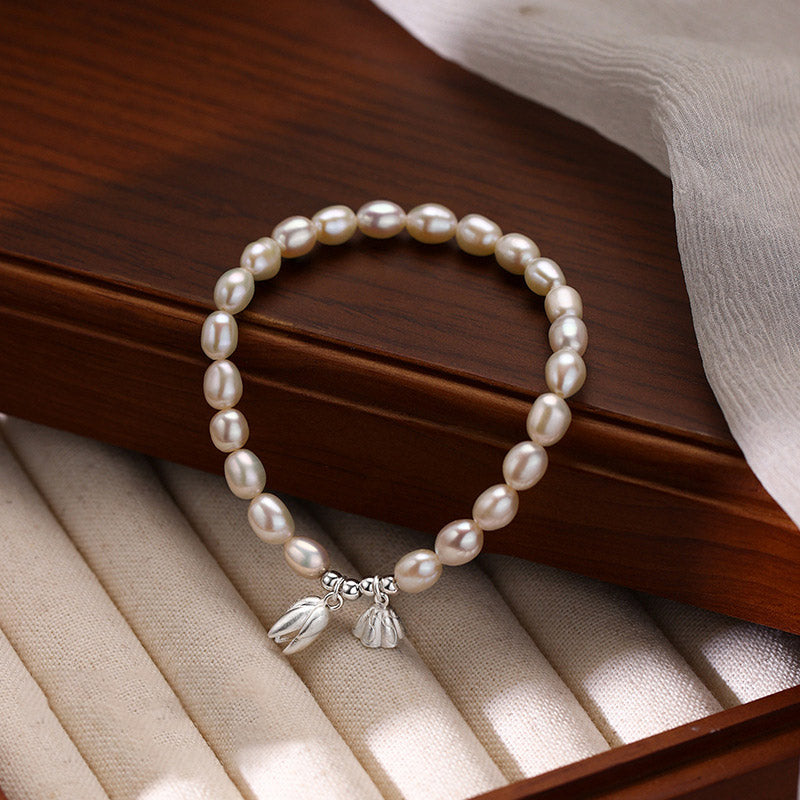 Elegantes Perlenarmband mit Silber Lotus Anhängern auf Holz.