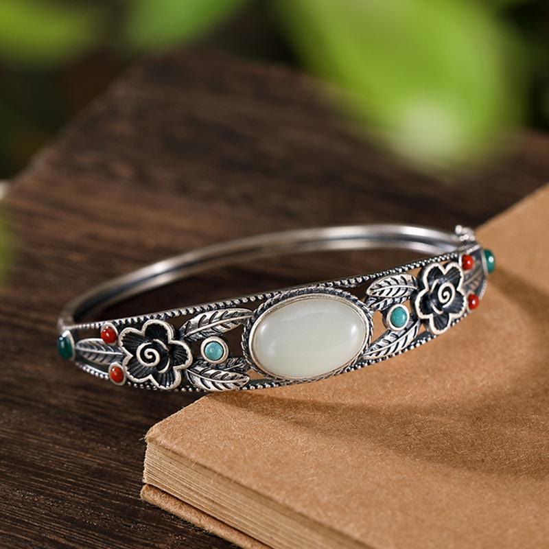 Silbernes Armband mit weißer Jade und bunten Steinen auf Buch.