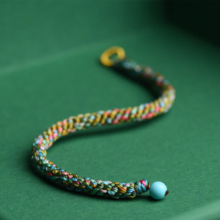 Buntes geflochtenes Armband mit Glücksperle auf grünem Hintergrund