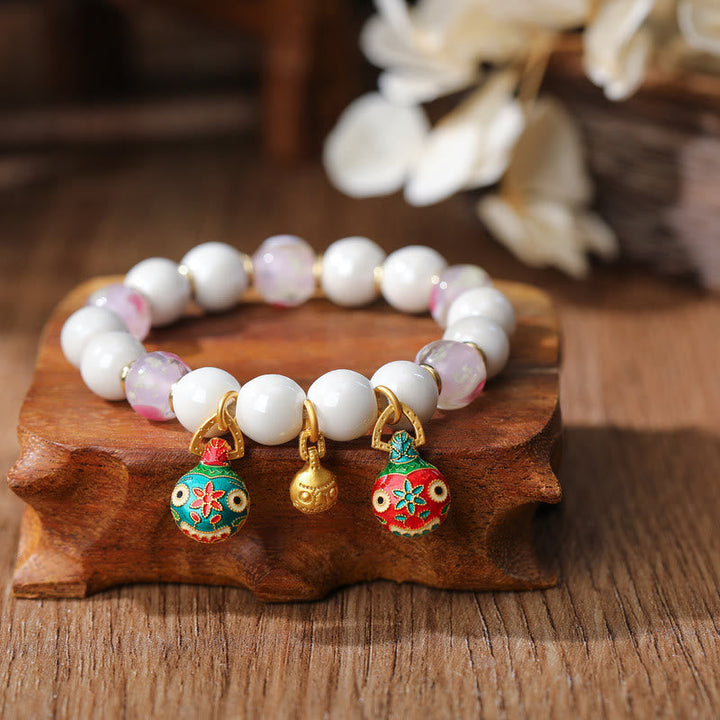 Weißes Perlen Armband mit bunten Glöckchen Anhängern auf Holz.