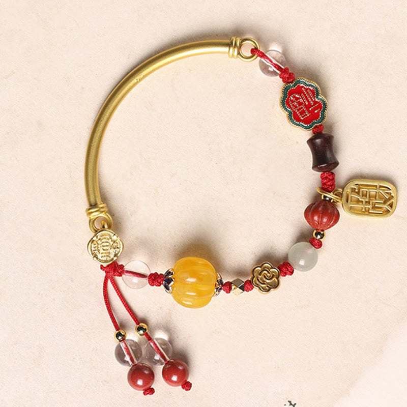 Armband Auspicious mit goldenen Elementen und roten Perlen elegant präsentiert.