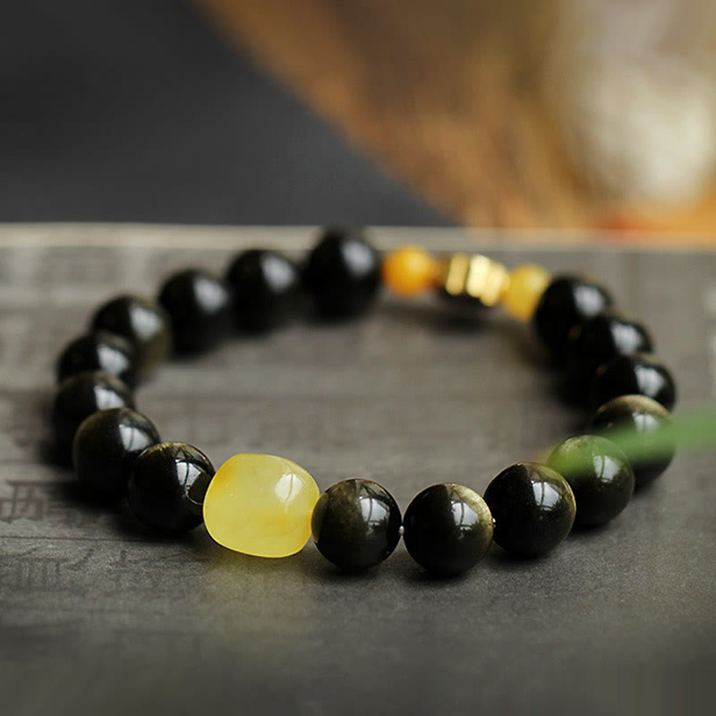 Schwarzes Obsidian Armband mit gelben Akzentsteinen auf grauem Untergrund.
