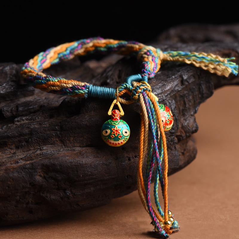 Buntes Armband mit Glöckchen auf dunklem Holz, mehrfarbige Schnüre.