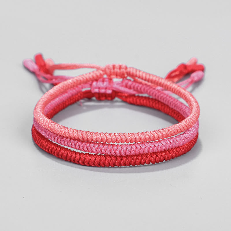 Drei geflochtene Armbänder in Rosa- und Rottönen, elastisch verknüpft.