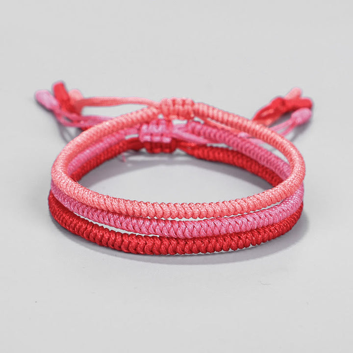Drei geflochtene Armbänder in Rosa- und Rottönen, elastisch verknüpft.
