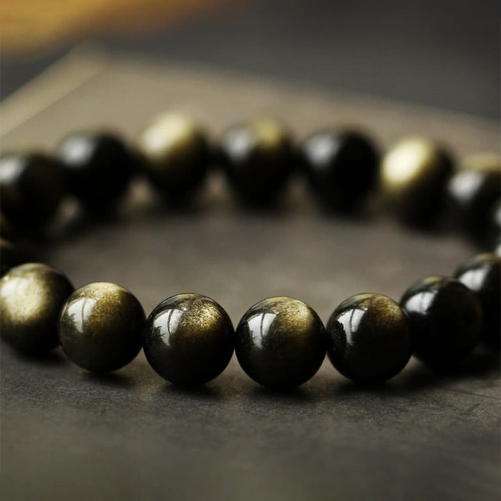 Schwarzes Obsidian Armband mit glänzenden Perlen auf grauem Untergrund elegant.