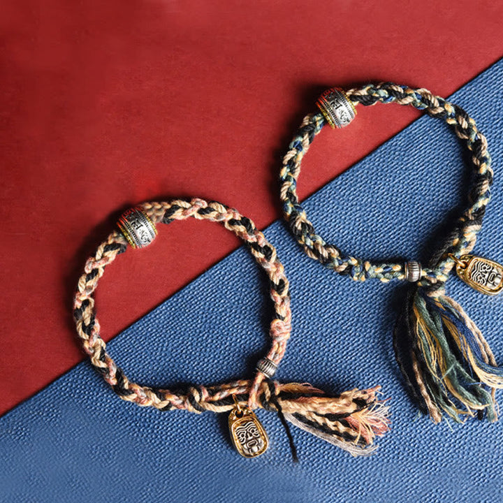 Geflochtenes Armband Om Mani Padme Hum mit Quasten auf blauem Hintergrund.