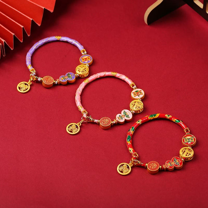 Armband – Glück & Wohlstand Energie mit goldenen Anhängern auf rotem Hintergrund.