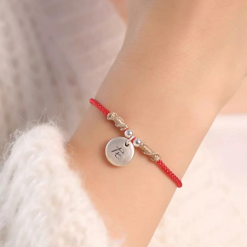 Rotes Armband mit silbernem Tierkreis-Anhänger am Handgelenk getragen.
