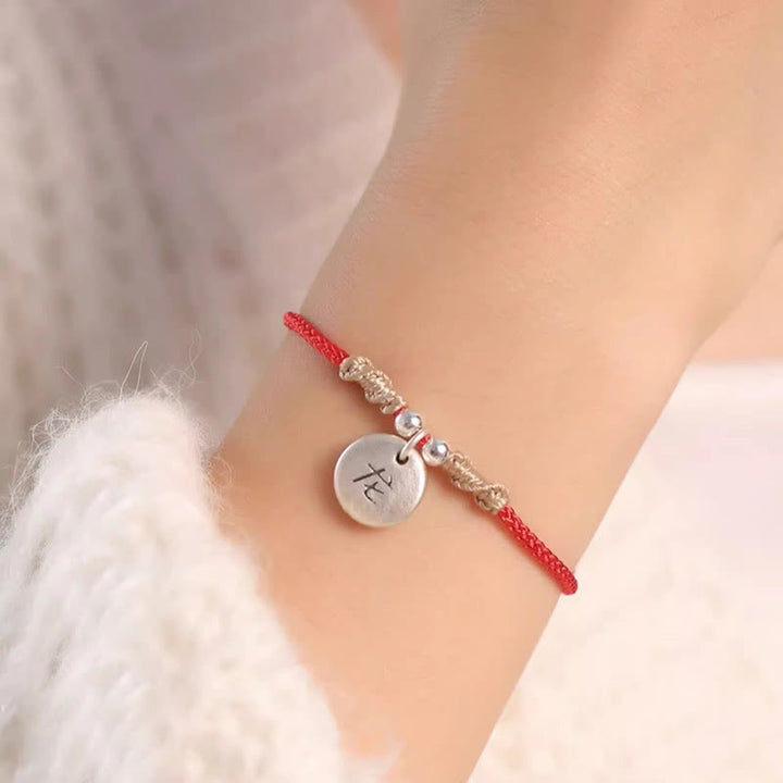 Rotes Armband mit silbernem Tierkreis-Anhänger am Handgelenk getragen.
